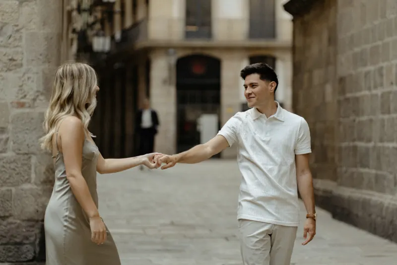 Couple smiling and holding hands while exploring a charming Barcelona alley during a Vacation Portraits photoshoot.