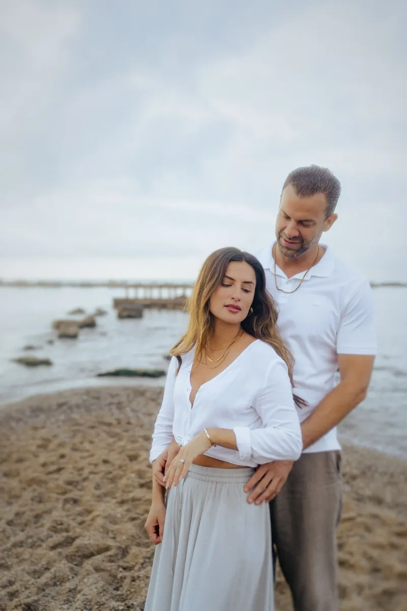 Couple standing close on a tranquil beach, sharing an intimate moment during a couples & engagements photoshoot.