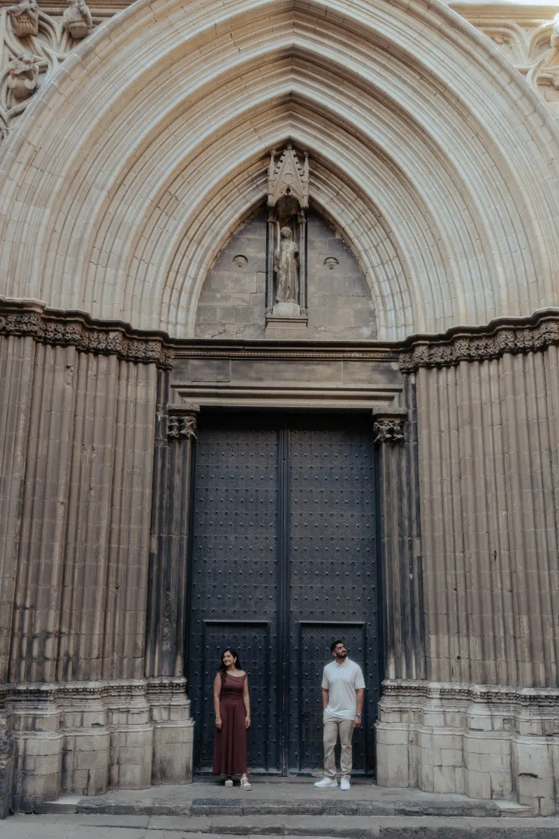 Couple stands apart, sharing a quiet moment in front of a grand gothic doorway during their engagement photoshoot.