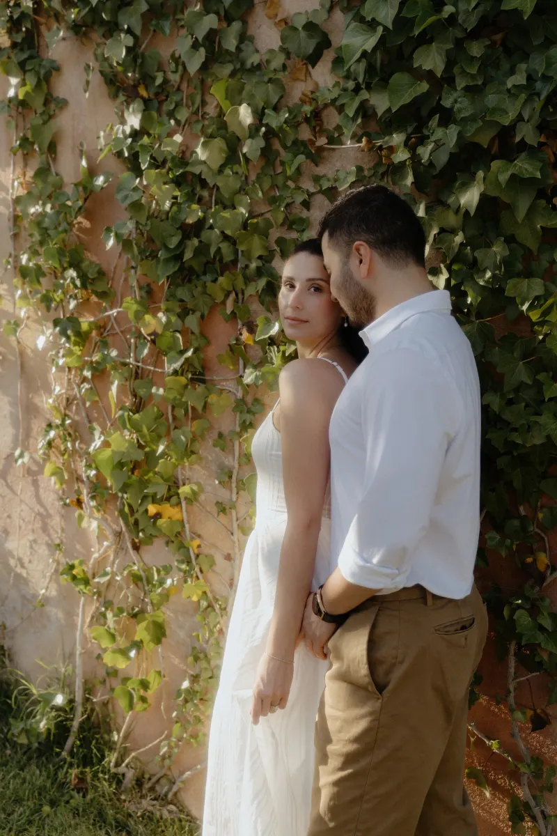 Couple stands close by a sunlit ivy wall, sharing a quiet, intimate moment during their couples & engagements photoshoot.