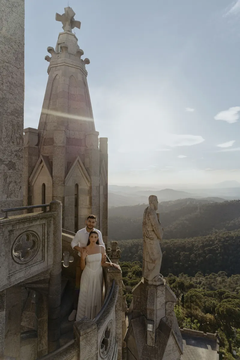 Couple stands close on a castle balcony at sunset, sharing a quiet moment during their engagement photoshoot.