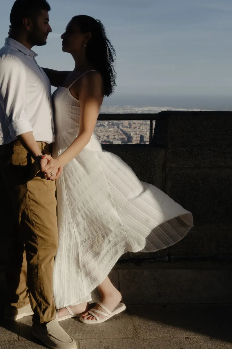 Couple stands close on a sunlit terrace overlooking the city, sharing an intimate moment during their engagement session.