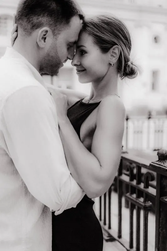 Couple stands close with gentle smiles, sharing a quiet, affectionate moment during an outdoor engagement photoshoot.