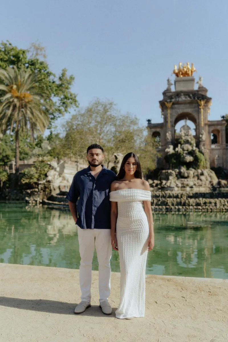 Couple stands side by side by a scenic fountain, sharing a calm moment during an outdoor engagement photoshoot.