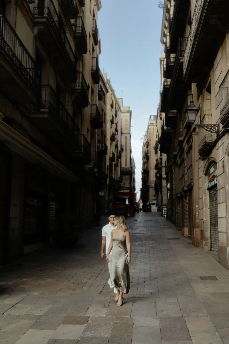 Couple strolling down a quiet Barcelona street, sharing a relaxed moment during their Vacation Portraits photoshoot.