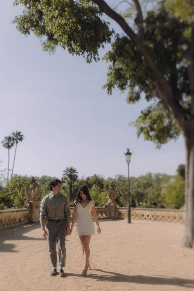 Couple strolling hand in hand through a sunlit garden, sharing a relaxed moment during an engagement photoshoot.