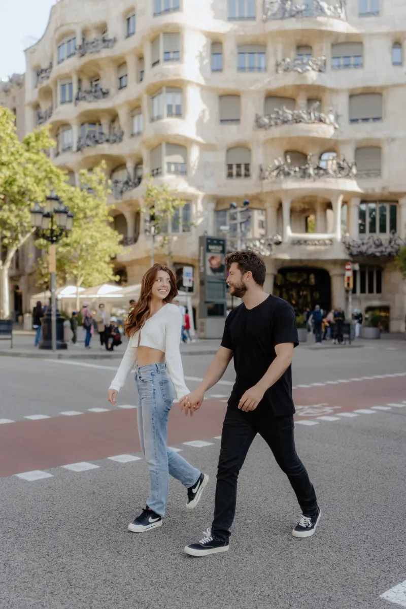 Couple strolls hand in hand across a city street, sharing a happy moment during a couples & engagements photoshoot.