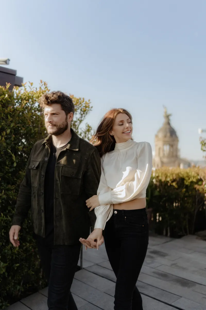Couple strolls hand in hand on a rooftop, sharing a lighthearted moment during an engagement photoshoot in the city.