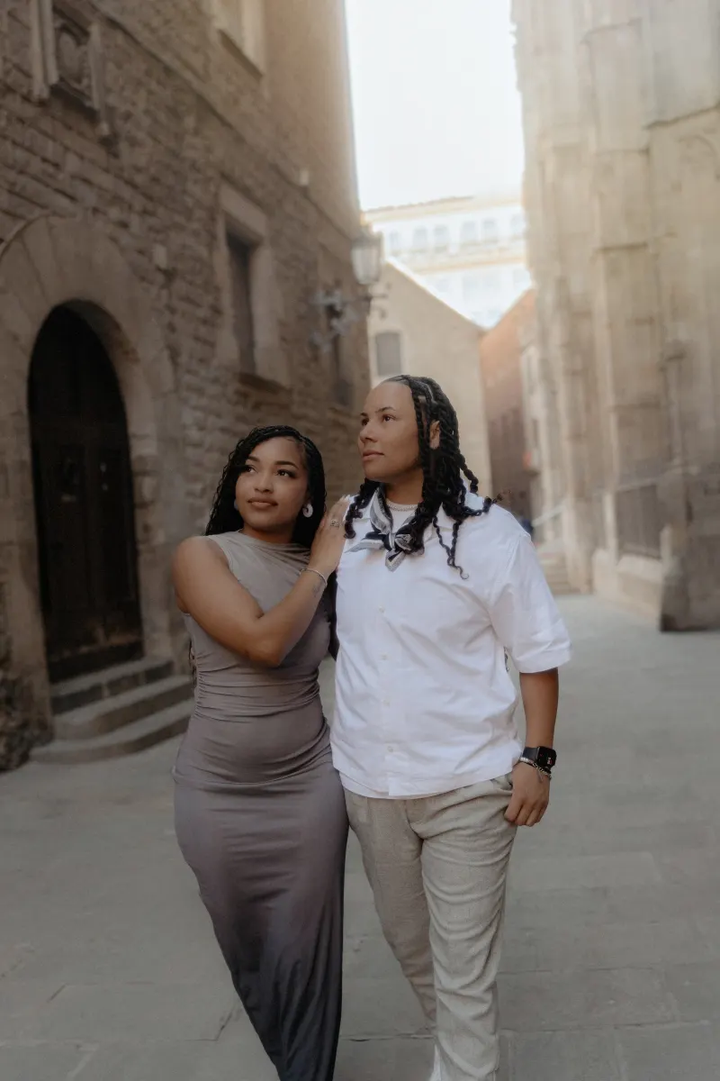 Couple strolls through a quiet Barcelona street, sharing a loving glance during their surprise proposal photoshoot.