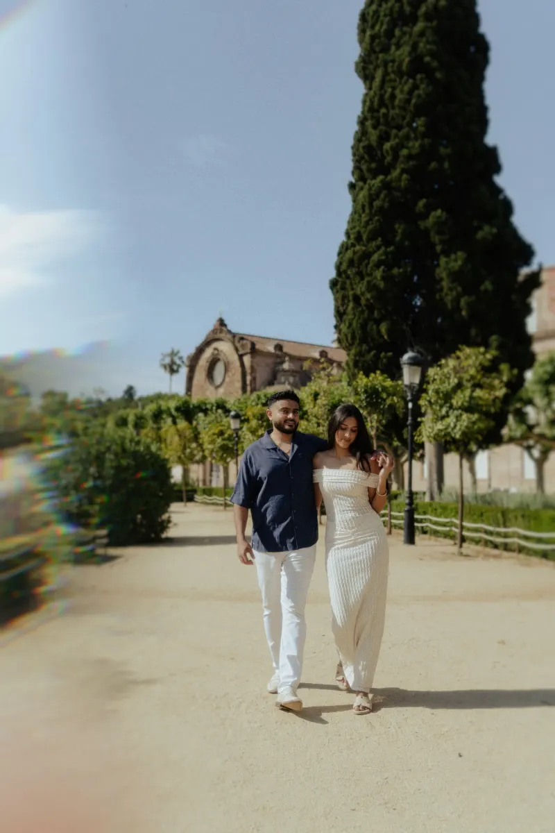 Couple walking arm in arm down a sunlit garden path, sharing a relaxed moment during a couples & engagements photoshoot.