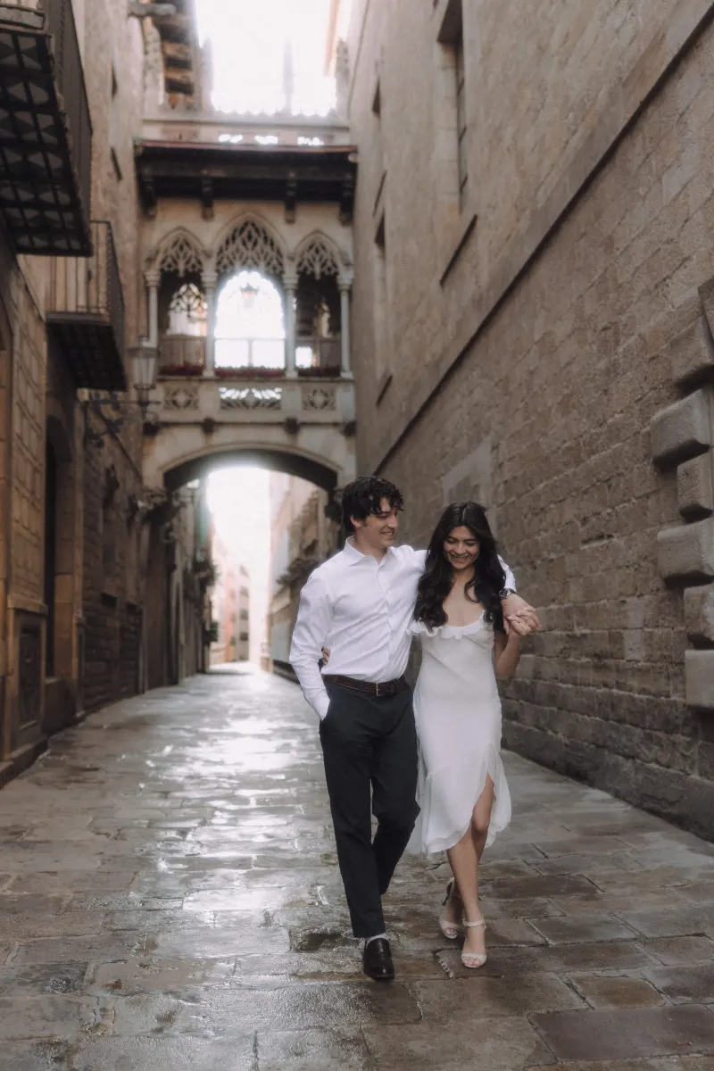 Couple walking arm in arm through a romantic Gothic Quarter street during a couples & engagements photoshoot.