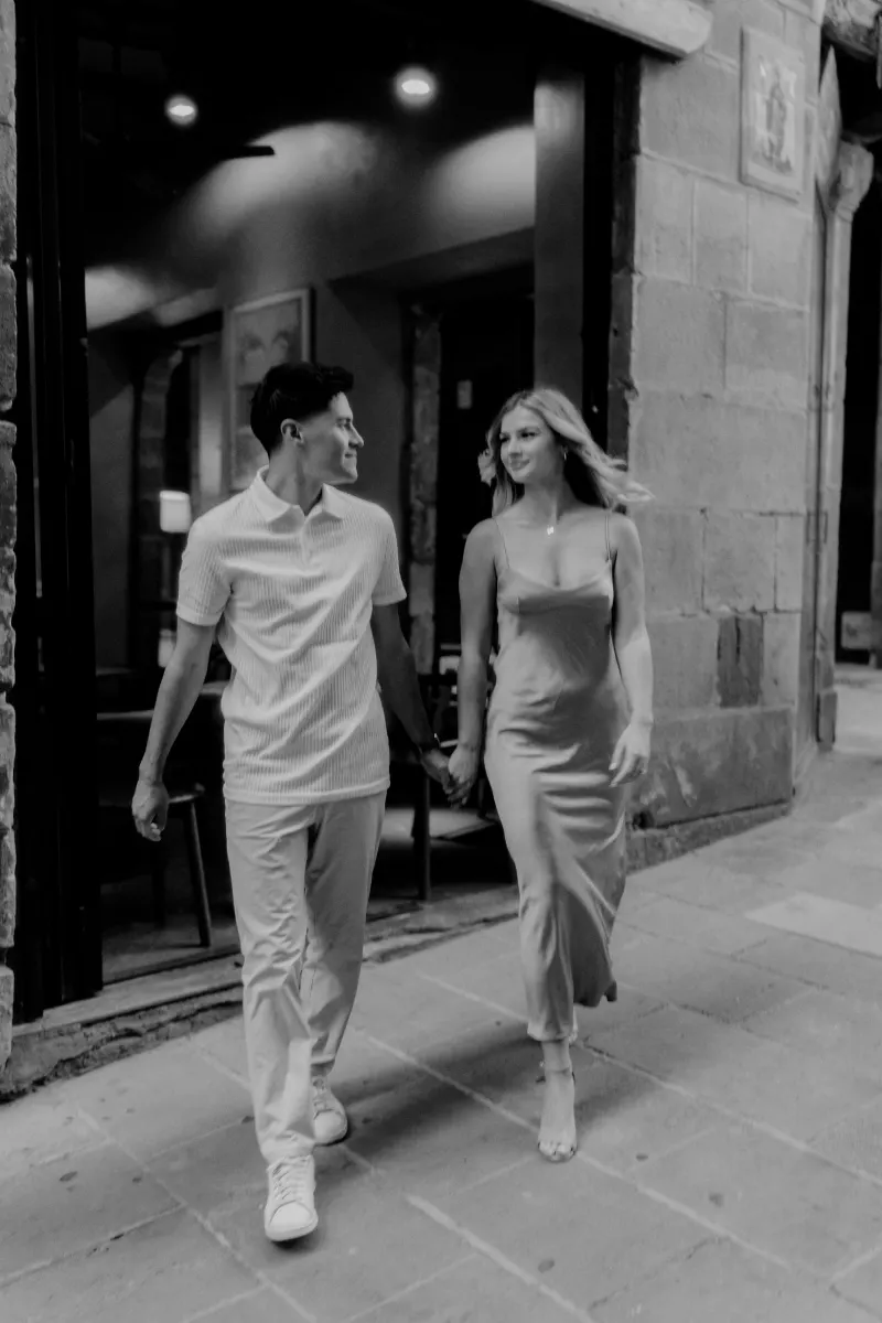 Couple walking hand in hand and smiling at each other on a Barcelona evening during a Vacation Portraits photoshoot.