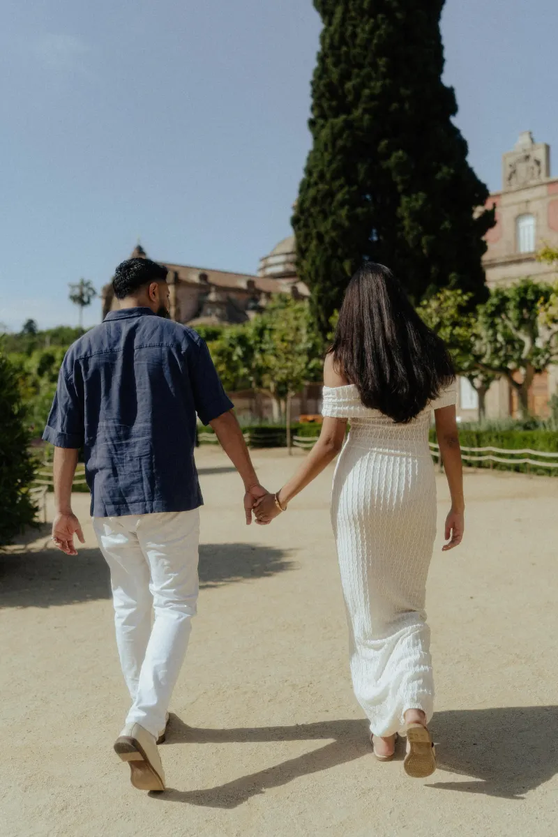Couple walking hand in hand down a sunlit garden path during a relaxed couples & engagements photoshoot in Barcelona.