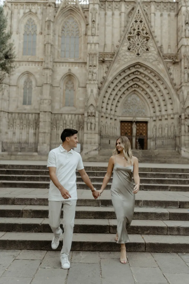 Couple walking hand in hand down cathedral steps in Barcelona, sharing a happy moment during a Vacation Portraits shoot.