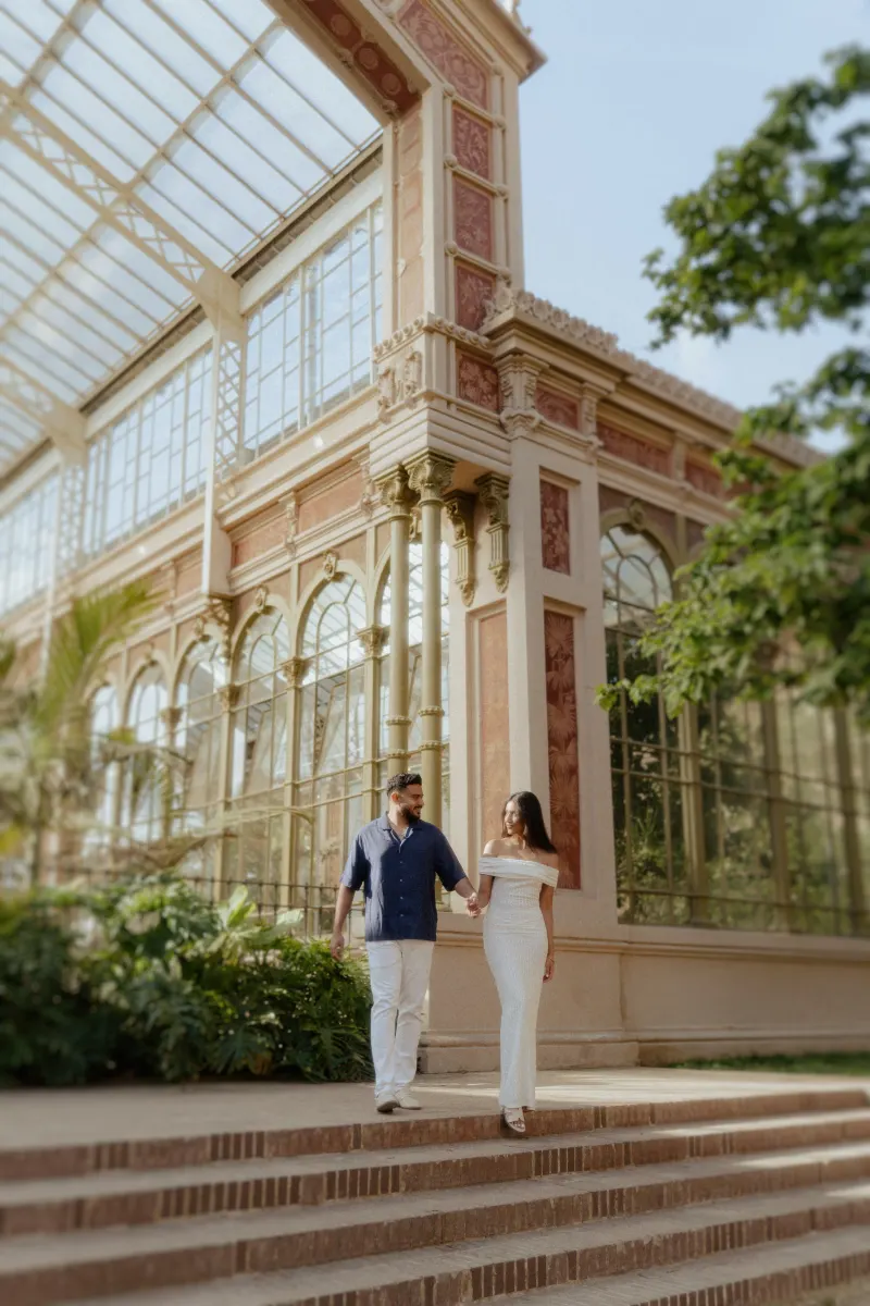 Couple walking hand in hand down garden steps, sharing a joyful moment during an engagement photoshoot at a glass conservator
