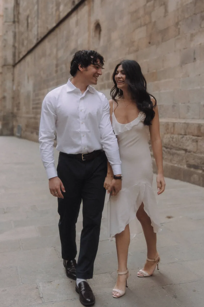 Couple walking hand in hand, sharing a joyful smile during a couples & engagements photoshoot in a historic city street.