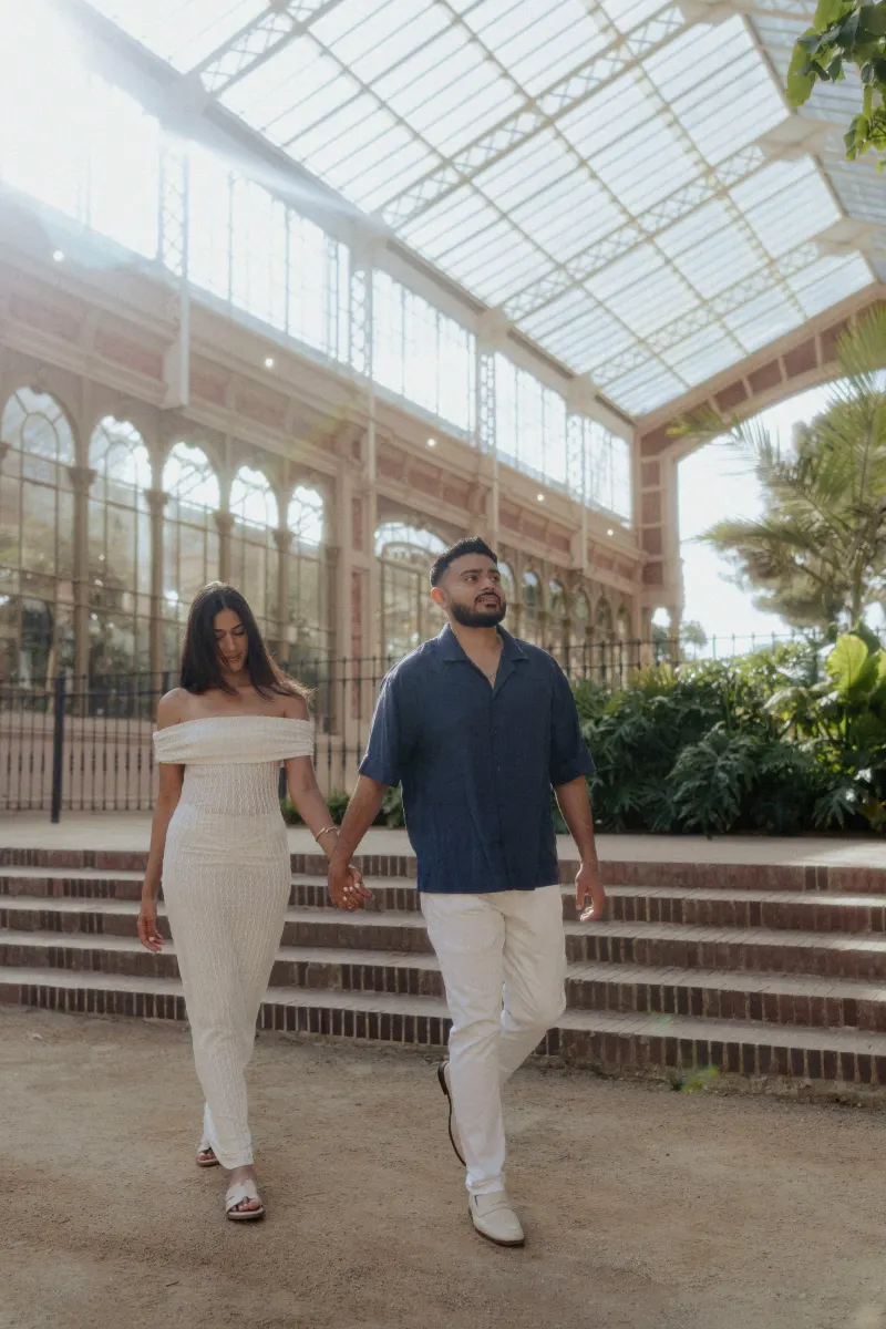 Couple walking hand in hand through a sunlit conservatory, captured during a relaxed engagement photoshoot.