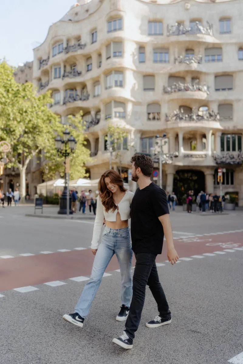 Couple walks arm in arm, laughing together on a sunny city street during a couples & engagements photoshoot.
