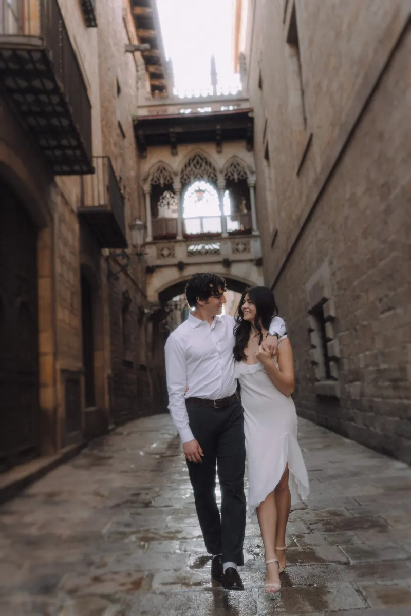 Couple walks arm in arm, smiling at each other on a charming Gothic Quarter street during an engagement photoshoot.