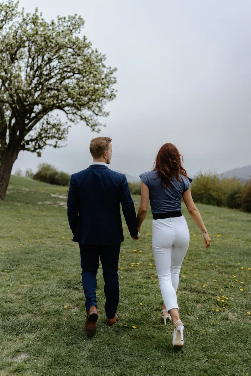 Couple walks hand in hand across a grassy hillside, sharing a quiet moment before their surprise proposal photoshoot.