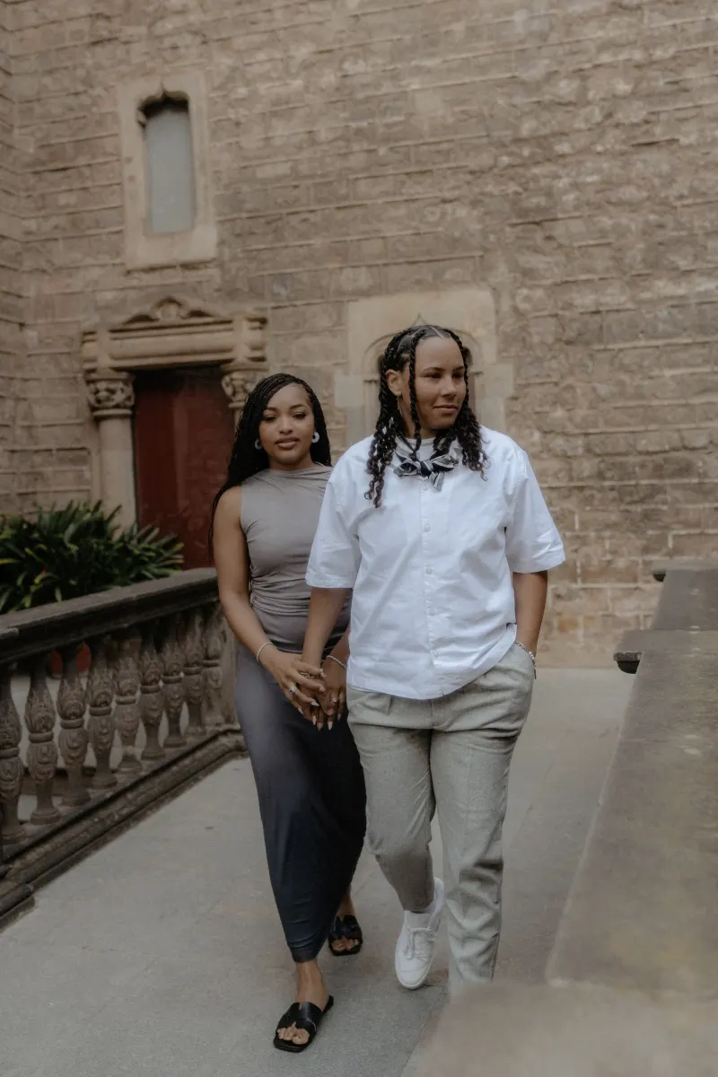 Couple walks hand in hand along a historic stone walkway in Barcelona during a surprise proposal photoshoot.