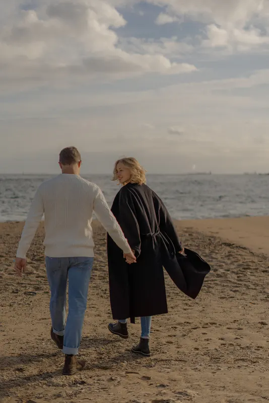 Couple walks hand in hand along the Barcelona beach, sharing a quiet moment during a couples & engagements photoshoot.
