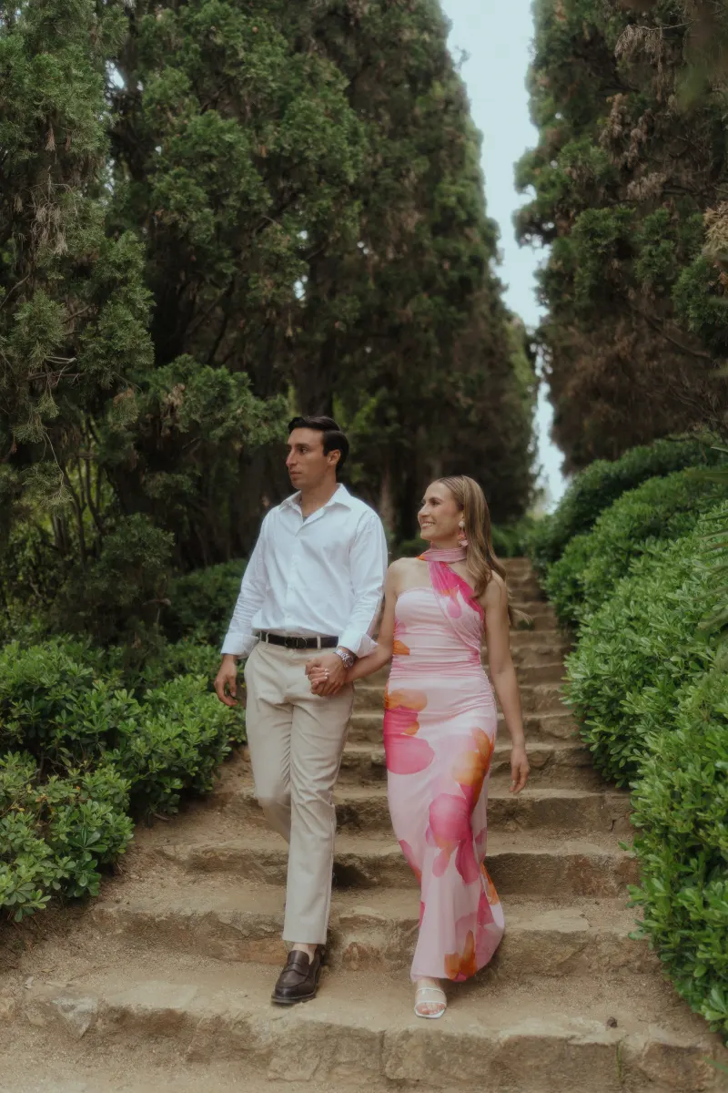 Couple walks hand in hand down stone steps through lush greenery during a surprise proposal photoshoot.