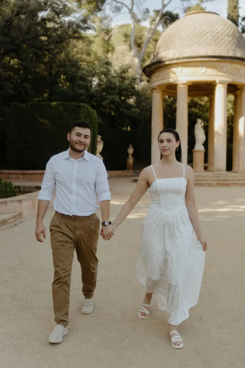 Couple walks hand in hand near a classical pavilion, sharing a relaxed moment during their engagement photoshoot.