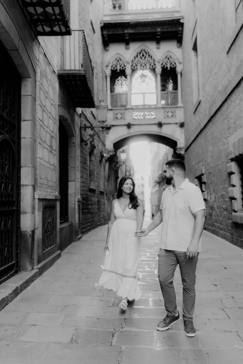 Couple walks hand in hand through a historic stone alley, sharing a happy moment during their engagement photoshoot.