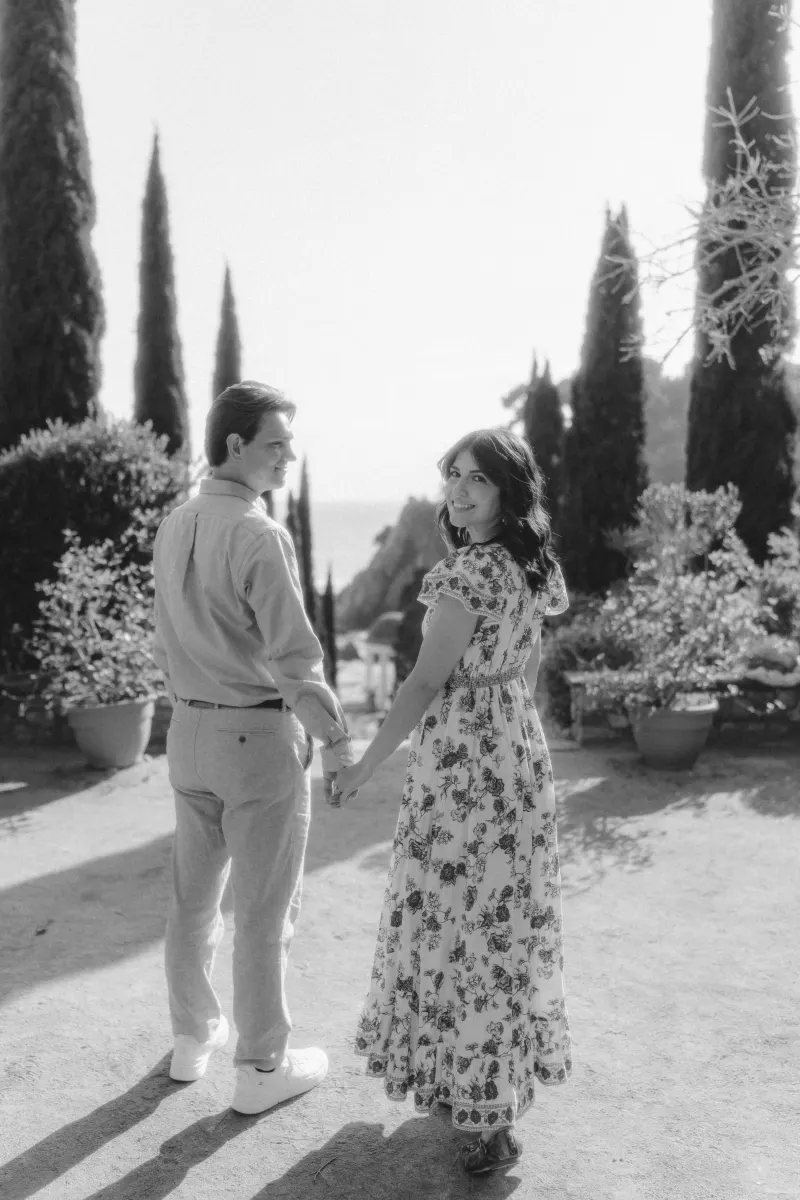 Couple walks hand in hand through a sunlit garden, sharing a joyful moment during a surprise proposal photoshoot.
