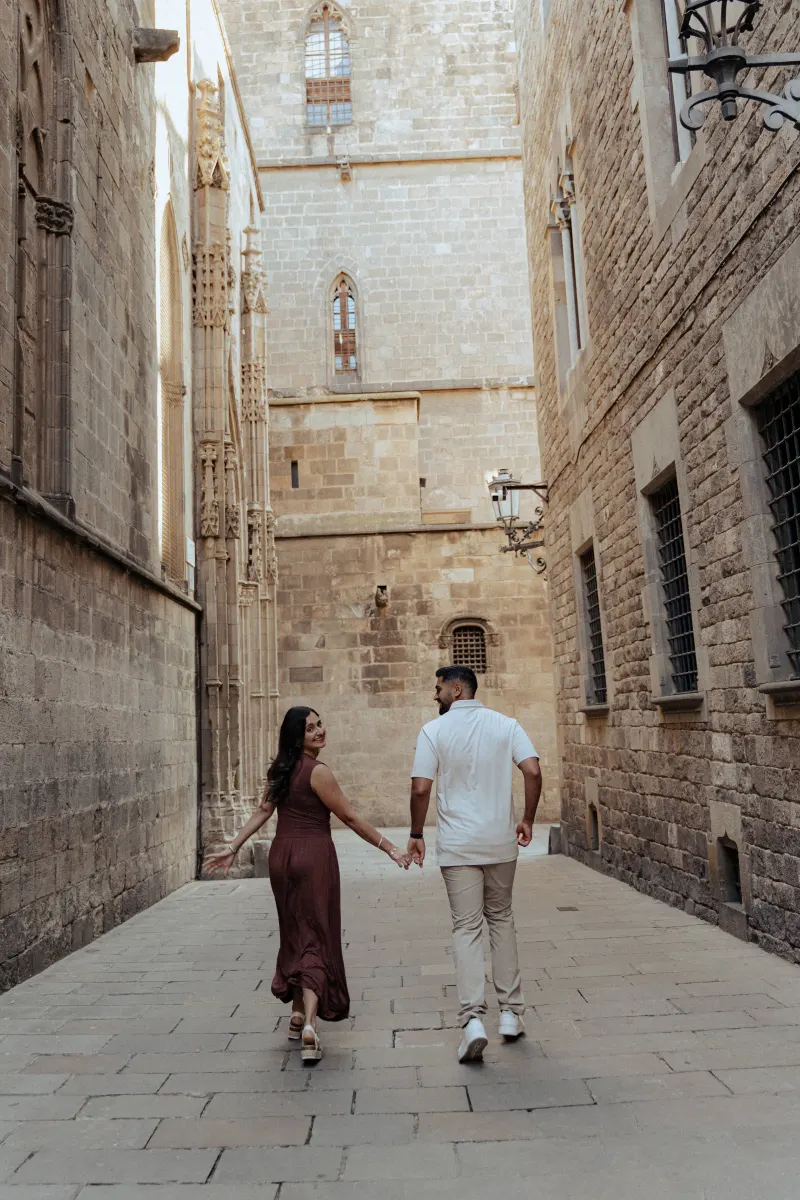 Couple walks hand in hand through a sunlit historic alley, sharing a joyful moment during their engagement photoshoot.