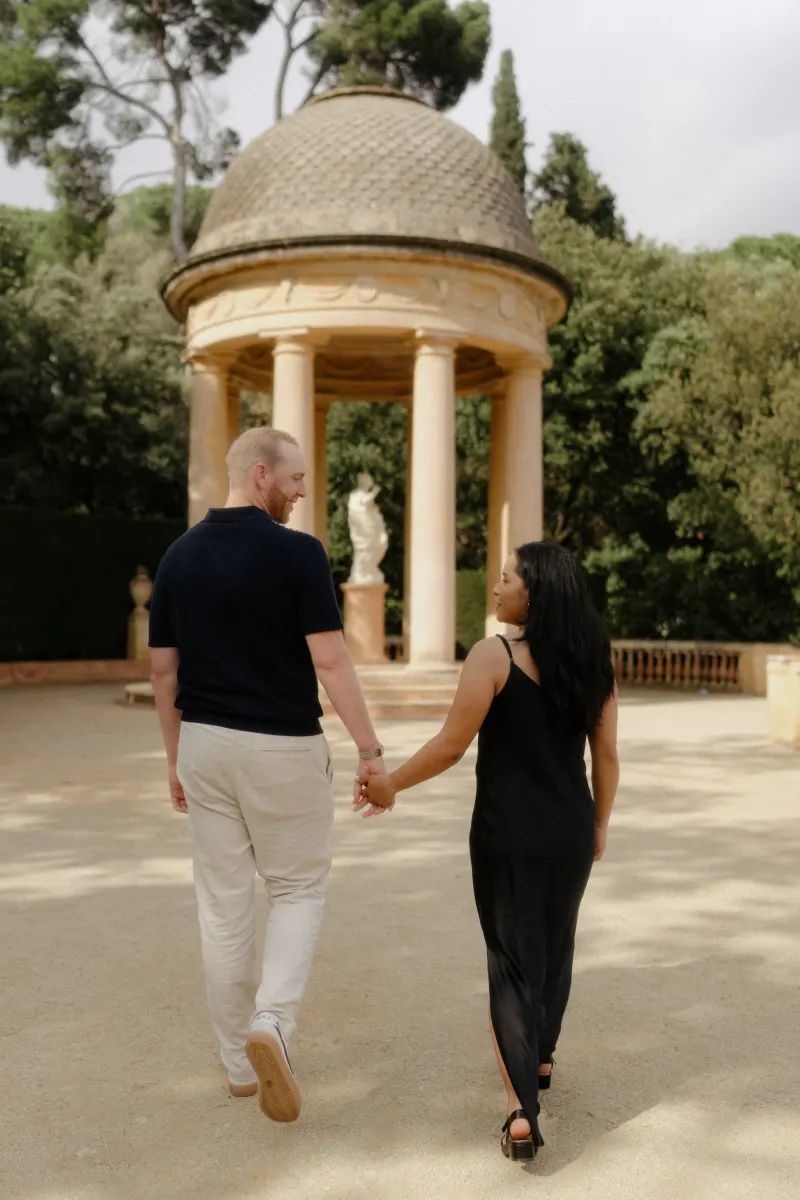 Couple walks hand in hand toward a garden pavilion, sharing a joyful moment during a surprise proposal photoshoot.