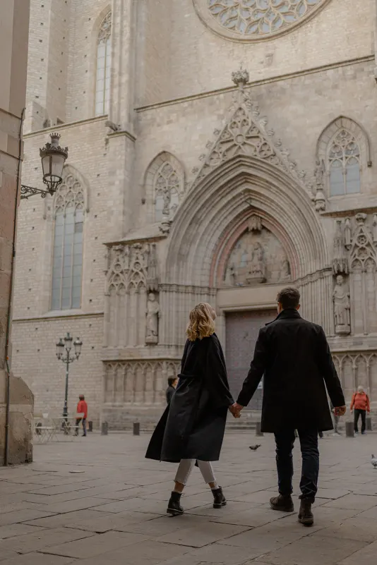 Couple walks hand in hand toward a historic Barcelona cathedral during a couples & engagements photoshoot.