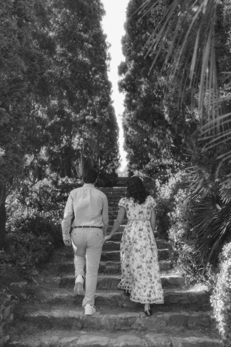 Couple walks hand in hand up stone steps through lush greenery, captured during a surprise proposal photoshoot.