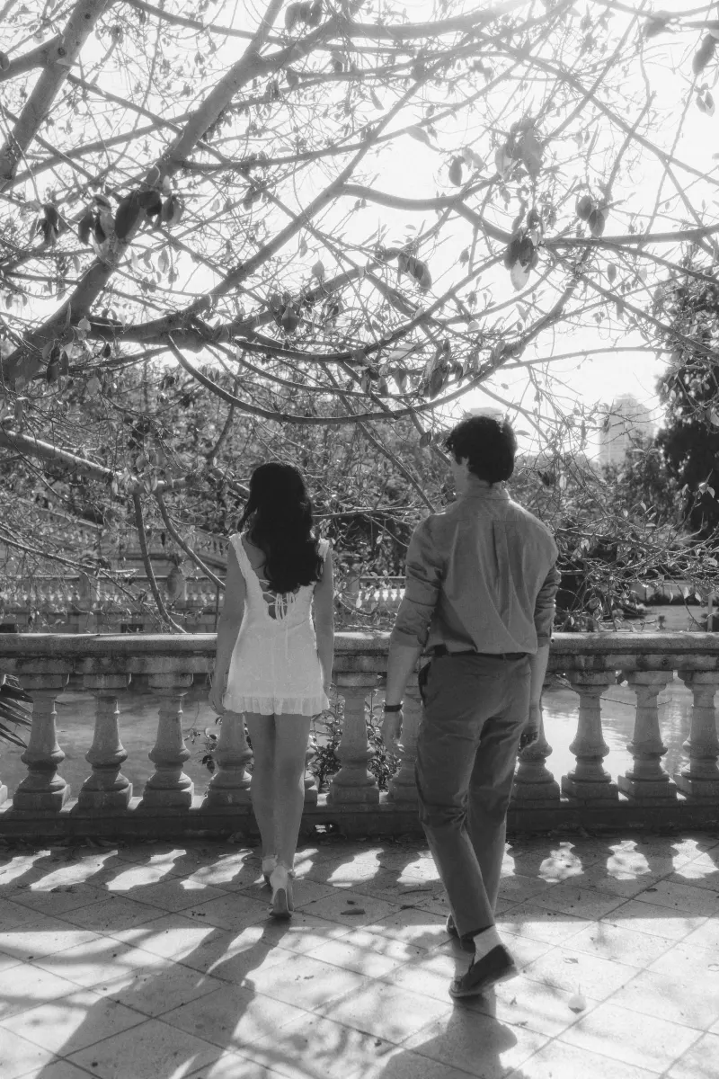 Couple walks side by side under leafy branches, enjoying a quiet moment during their engagement photoshoot outdoors.