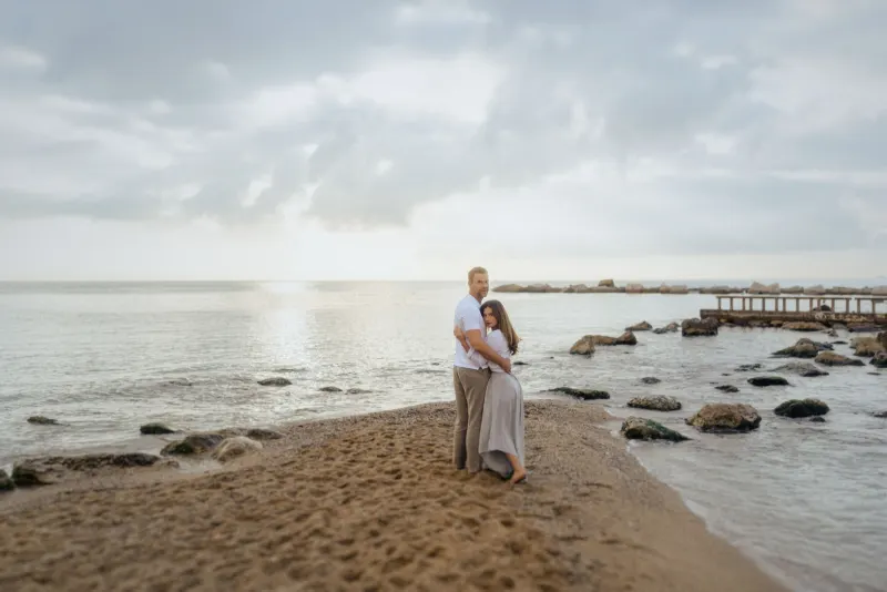 Couple wrapped in a loving embrace on a sandy beach at sunrise, captured during a couples & engagements photoshoot.