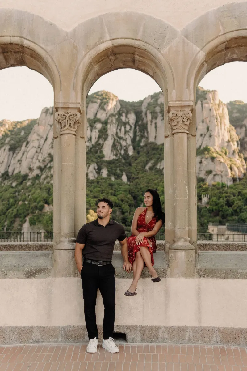 Dan and Sydney pose beneath carved arches with the Montserrat mountains framed behind them.