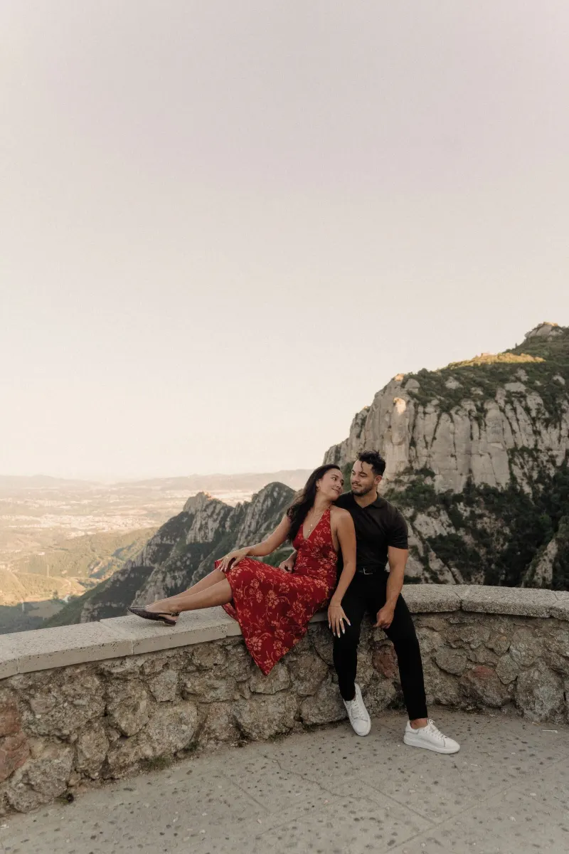 Dan and Sydney sit together on a stone wall with the Montserrat landscape behind them.