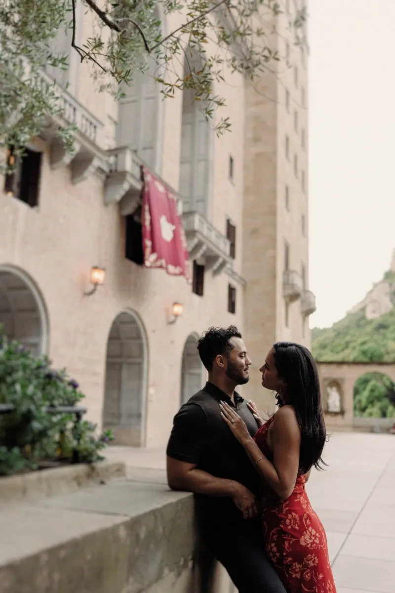 Dan and Sydney stand close beside the historic walls and flowers of Montserrat monastery.