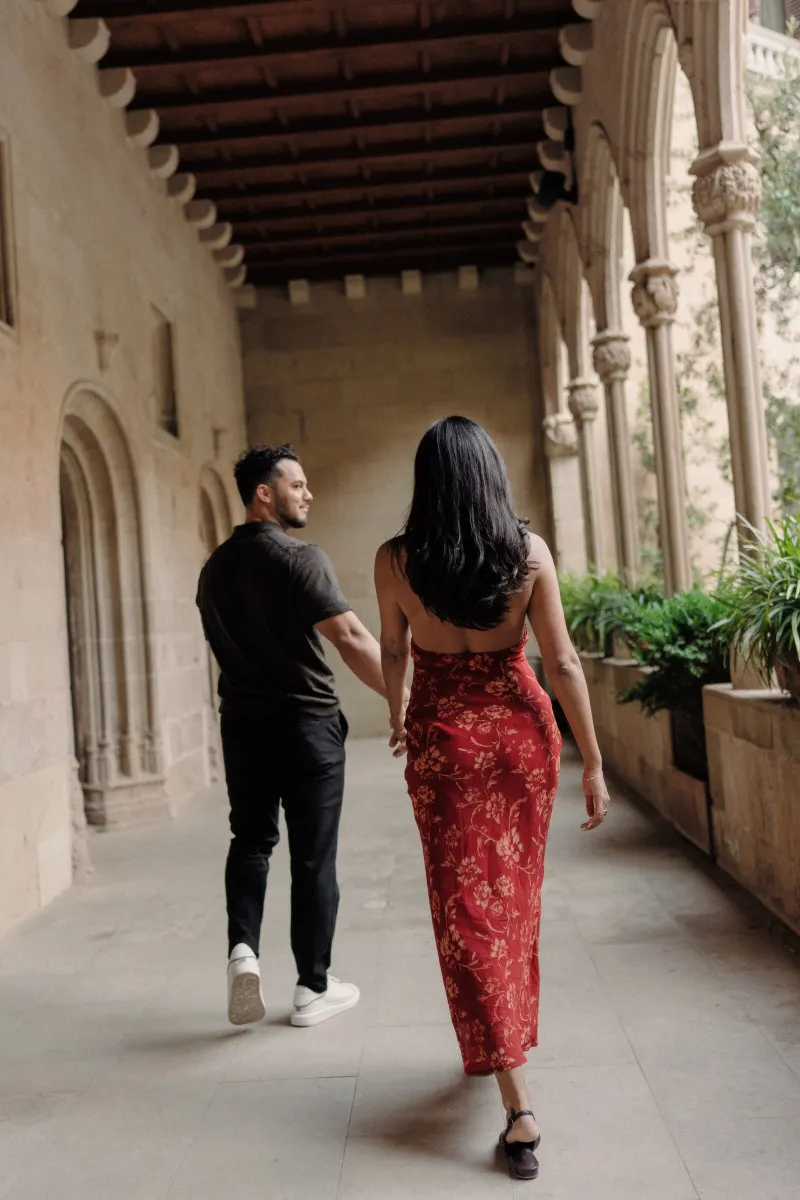 Dan and Sydney walk away hand in hand along a covered monastery gallery.