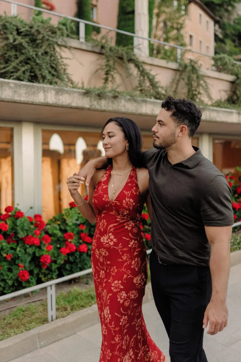 Dan and Sydney walk together past red flowers in the Montserrat monastery gardens.