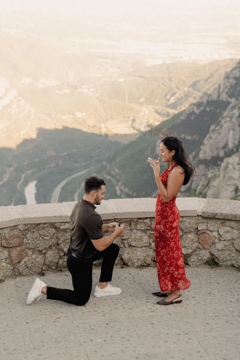 Dan drops to one knee as Sydney reacts with surprise above the Catalan landscape in Montserrat.