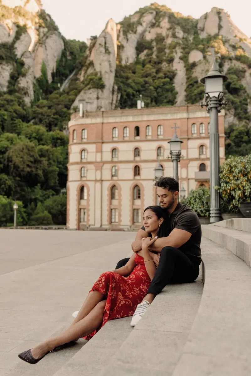 Dan embraces Sydney from behind in a wide seated portrait at Montserrat monastery.