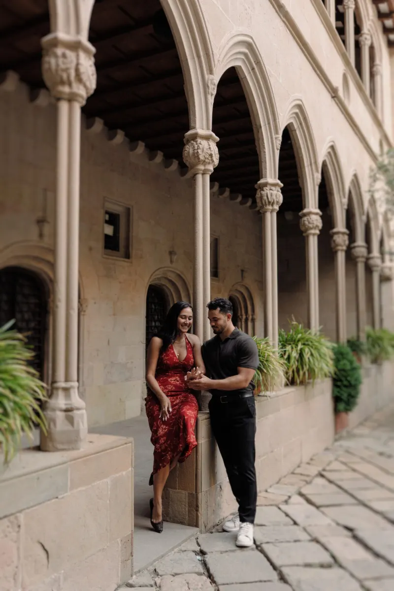 Dan helps Sydney sit along a stone cloister beneath Gothic arches in Montserrat.
