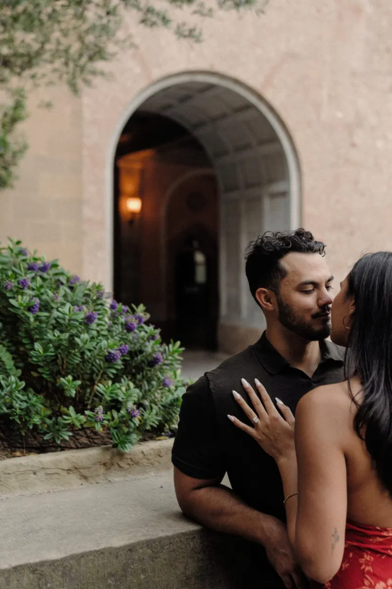 Dan kisses Sydney beside green shrubs and a rounded stone doorway in Montserrat.