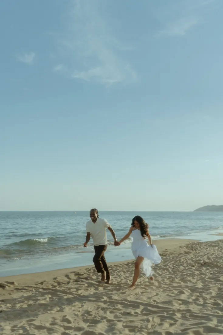 Dexter and Cheryl run hand in hand along Castelldefels Beach during their engagement photoshoot.