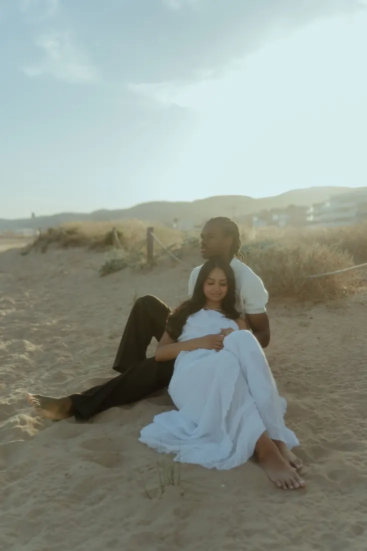 Dexter and Cheryl sit together among the dunes during a golden-hour engagement photoshoot in Castelldefels.