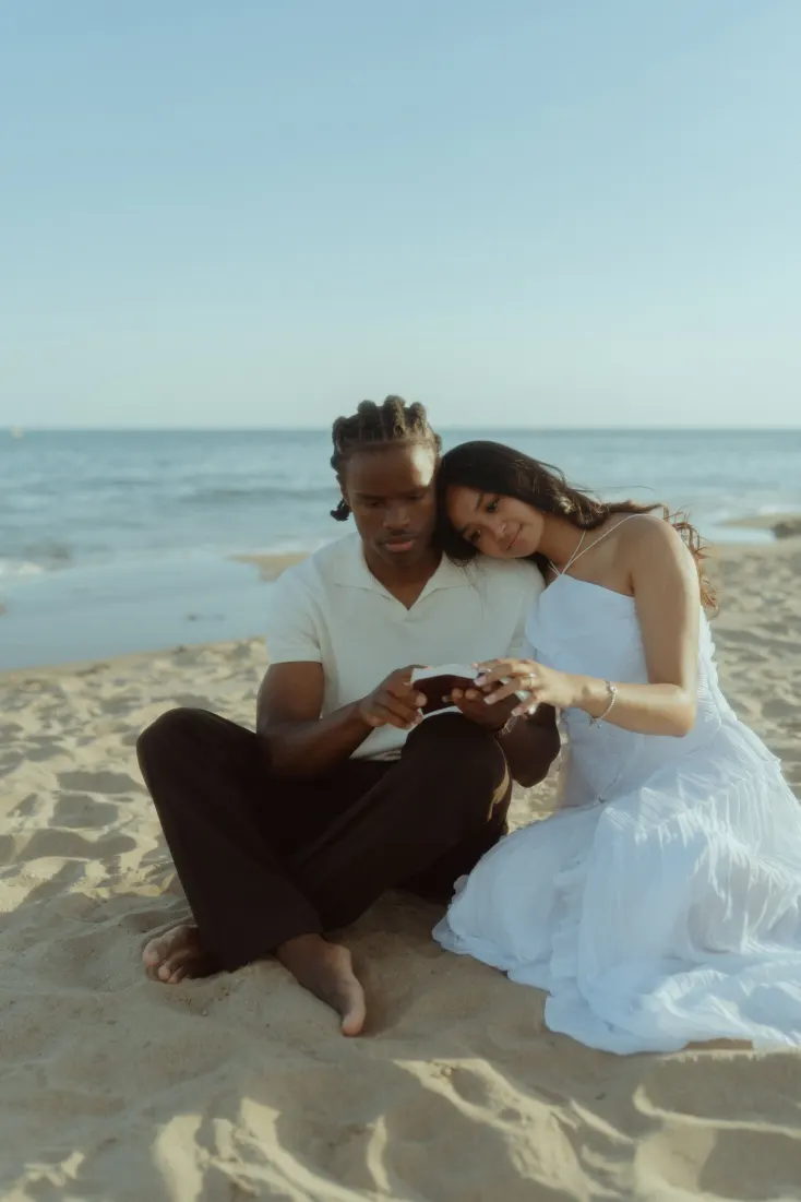 Dexter and Cheryl sit together on the sand and admire the engagement ring after the proposal.