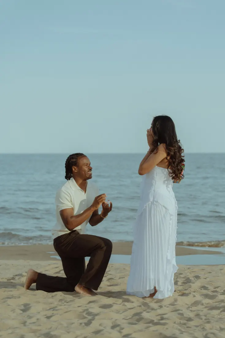 Dexter kneels with an engagement ring as Cheryl reacts during their Castelldefels Beach proposal.