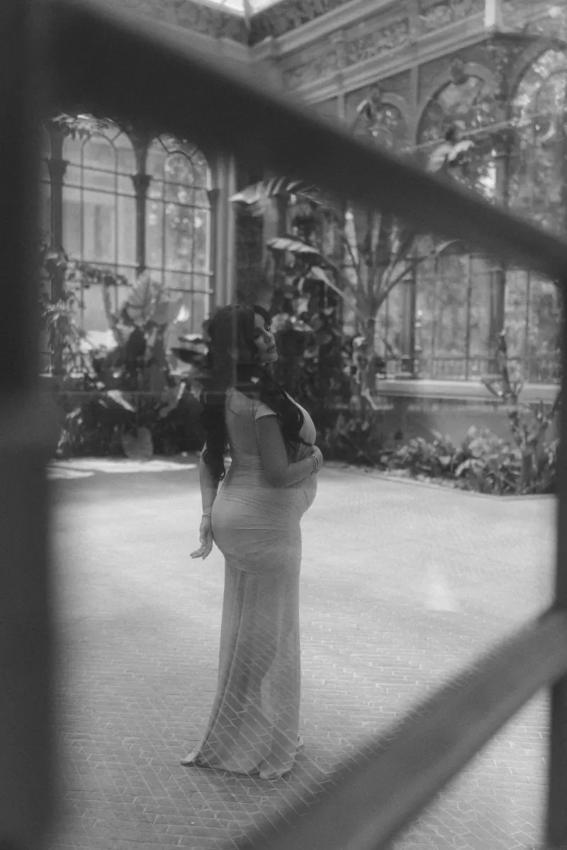Elegant expectant mother in a fitted dress poses in a sunlit conservatory, Vacation Portraits maternity session.